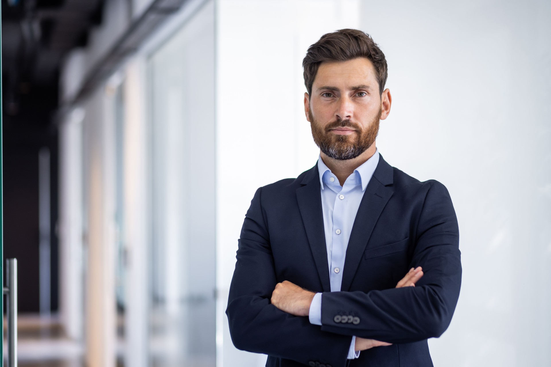 Portrait of serious self-confident male lawyer standing in office, crossed arms on chest and looking at camera